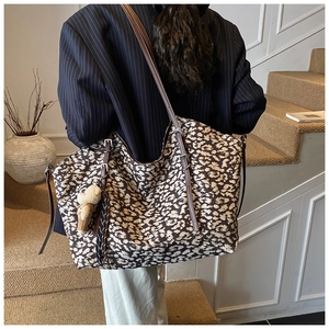Detail of leopard print tote bag featuring brown faux leather straps and a plush bear charm