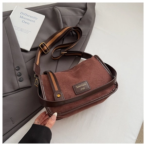 Close-up of brown suede bag with striped shoulder strap and logo detail