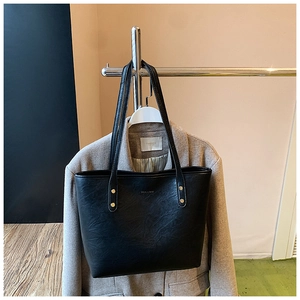 Detail shot of black leather tote bag with gold rivets on oatmeal wool coat background