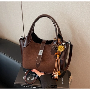 Detailed close-up of brown suede bucket bag featuring silver twist-lock and tassel charm