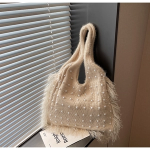 Detailed texture of cream knit tote bag with pearl accents and long bohemian tassels
