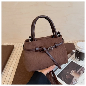 Close-up of brown suede bucket bag featuring metal buckle and leather handle in a lifestyle setting