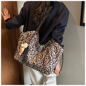 Detail of leopard print tote bag with brown leather strap and plush bear charm