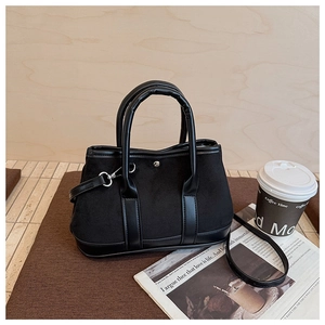 Detail of black suede tote bag with leather trim and metal clasp on woven mat