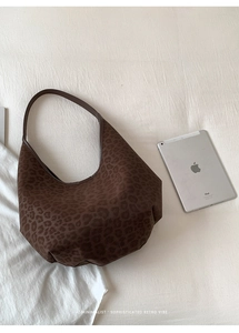 Detailed close-up of brown leopard print Hobo bag on white fabric with casual props