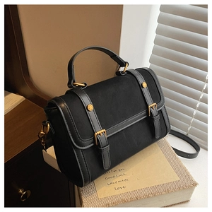 Detail of vintage black messenger bag with leather straps and gold rivets on a book
