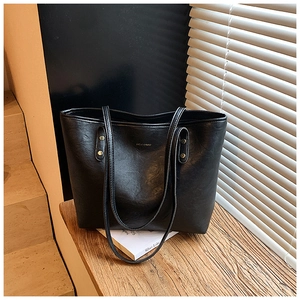 Close-up of black PU leather tote bag with gold logo on wood stairs with window shadows