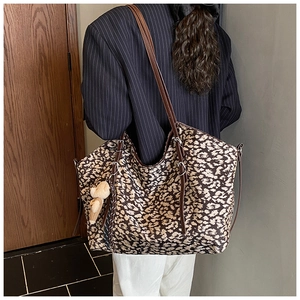 Detail of leopard print tote bag with brown leather straps and a plush bear pendant