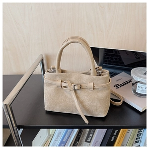 Detail of beige suede trapezoid handbag featuring a decorative buckle and matte texture