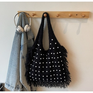 Detailed macro view of black knitted tote bag featuring white faux pearls and long fringe