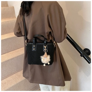 Détail d'un sac seau en peluche noire avec breloque doudou et bandoulière en cuir