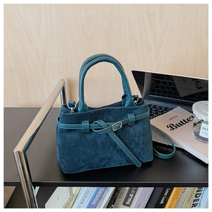 Detail of dark blue suede handbag with metallic buckles in an office setting