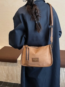 Retro brown suede crossbody bag with wide striped strap worn by model in dark blue coat