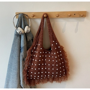 Detail of brown knitted tote bag featuring white pearl accents and long bohemian tassels