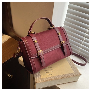 Detail view of burgundy leather handbag with suede texture and gold buckle accents