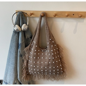 Detail of a brown knitted tote bag with white pearl accents and fringe bohemian edges