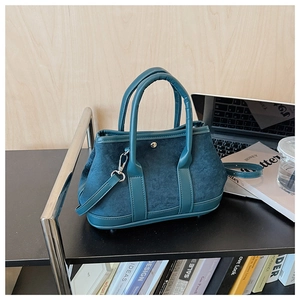 Macro shot of teal suede tote bag featuring silver metal buckle in a home office setting