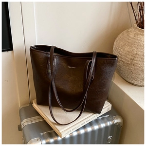 Detail of a large dark brown tote bag on a suitcase showing the leather texture and logo