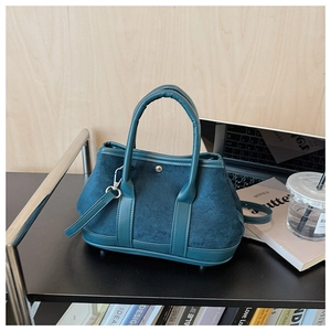 Detail of teal faux suede handbag with silver buckle on a minimalist desk setting