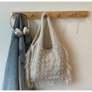 Detail of a creamy white knit tote bag with pearls and fringe on a wooden hanger