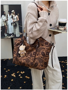 Detail of vintage paisley tote bag with brown straps and stylish bear charm on display