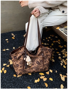 Detail view of brown paisley canvas tote bag with leather strap and plush bear charm