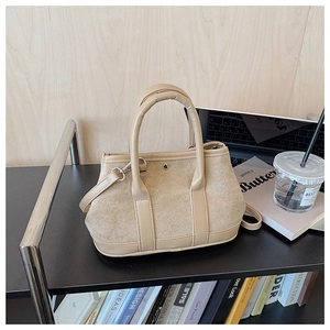 Detail view of a beige suede and leather tote bag styled on a sleek modern office shelf