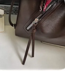 Close-up of smooth metal zipper and long leather puller on a dark brown tote bag