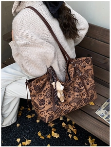 Brown paisley tote bag with leather strap and bear charm in a scenic autumn park setting