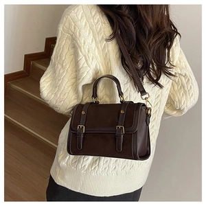 Detail view of a vintage dark brown leather crossbody bag styled with a white knit sweater