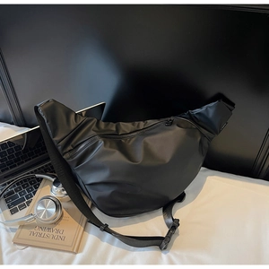 Detail of minimalist black nylon crescent bag with adjustable strap on white bedding