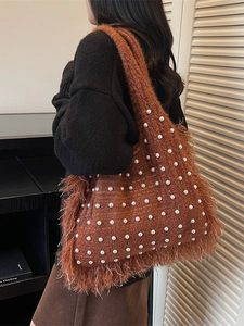 Brown knitted tote bag with white pearl accents and long tassels worn on shoulder