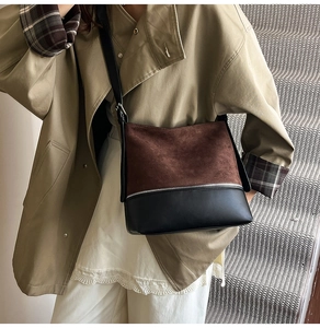 Model wearing a brown suede and black leather bucket bag on a neutral grey staircase