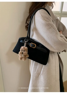 Dettaglio borsa a conchiglia nera opaca con ciondolo a cucciolo su un trench beige