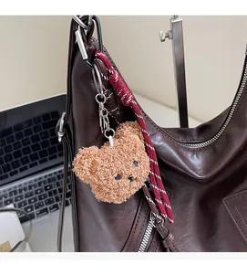 Brown fluffy bear plush charm detail with woven cord on a leather tote bag
