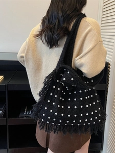 Black knitted tote bag with white pearl accents and fringe detail worn by a model