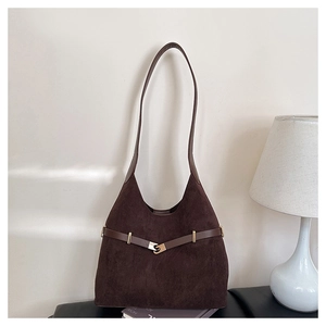 Detail of dark brown suede hobo bag with gold S-shaped buckle on dark books