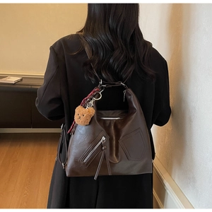 Detail of dark brown Hobo bag with plush bear charm and checkered ribbon on shoulder strap