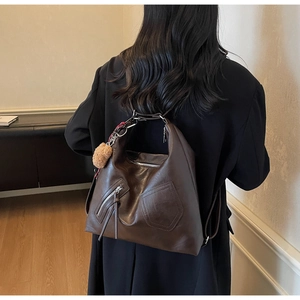 Macro detail of deep brown faux leather hobo bag with zip pockets and plush ball pendant