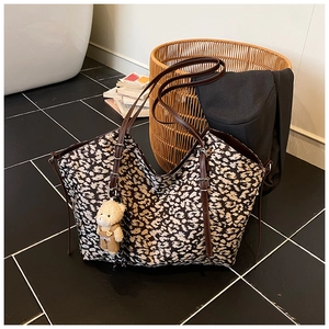 Detail of leopard print tote bag featuring leather handles and cute teddy bear charm