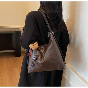 Brown soft leather tote bag detail with decorative stitching and plush bear charm accessory