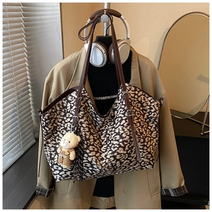 Macro detail of large leopard print tote bag with brown straps and plush bear charm