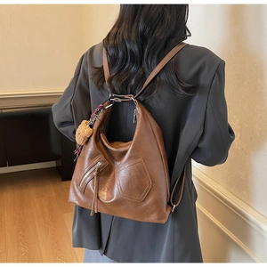 Detail of vintage brown PU leather backpack with teddy bear charm and plaid scarf