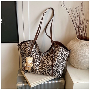 Detail of leopard print tote bag with bear charm on a vintage suitcase background