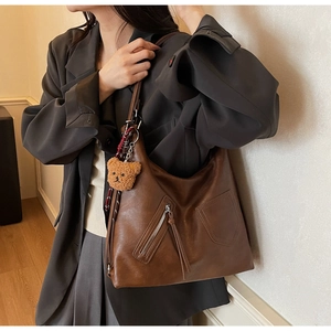 Detail of vintage brown leather hobo bag with zip pocket and cute plush bear charm