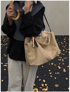 Detail of camel canvas tote with wooden bead charm and black leather strap in autumn setting
