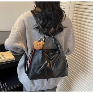 Rear view of black soft leather tote bag with brown bear charm and ribbon on model