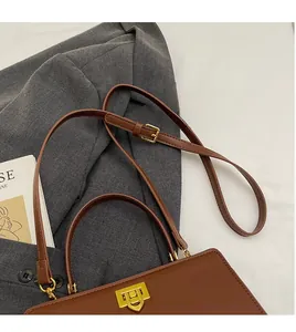 Détail d'un sac en cuir mat marron avec fermoir tournant doré et bandoulière amovible