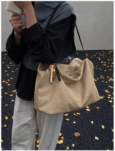Detail of a large khaki canvas tote bag with black leather straps and beaded pendant