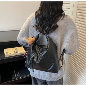 Rear view of a black matte leather backpack with a brown plush bear charm and side pocket